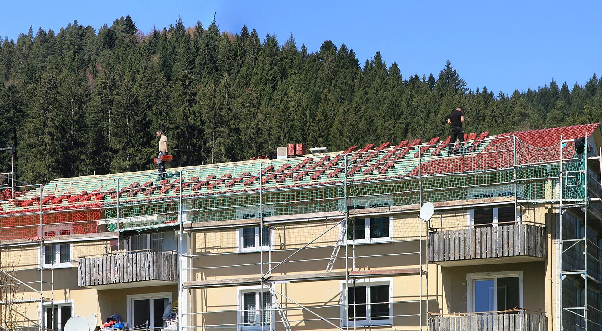 Takarbete på ett flerbostadshus med byggställning runt fasaden